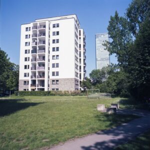 Ein mehrstöckiges Wohnhaus mit umliegender Rasenfläche, dahinter ein Hochhaus.